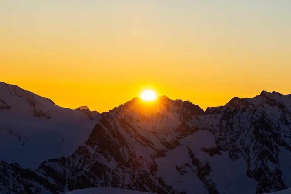 Sunrise over snow-capped mountains with clear sky.